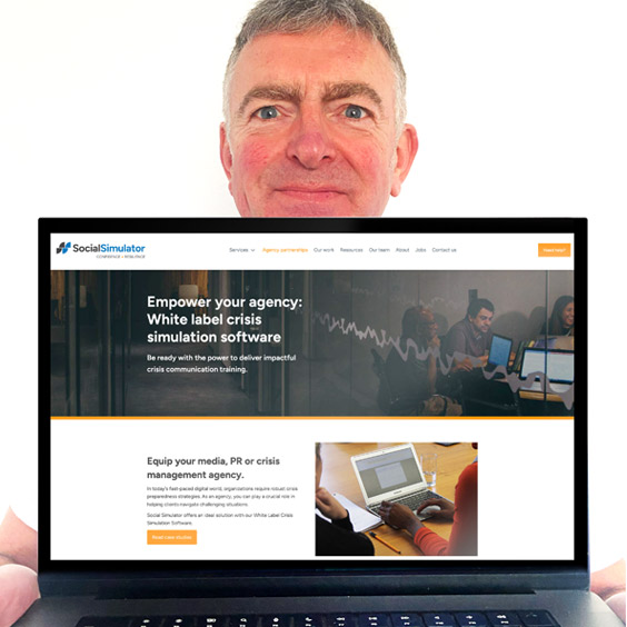 Mark holding a laptop showing the Social Simulator website design